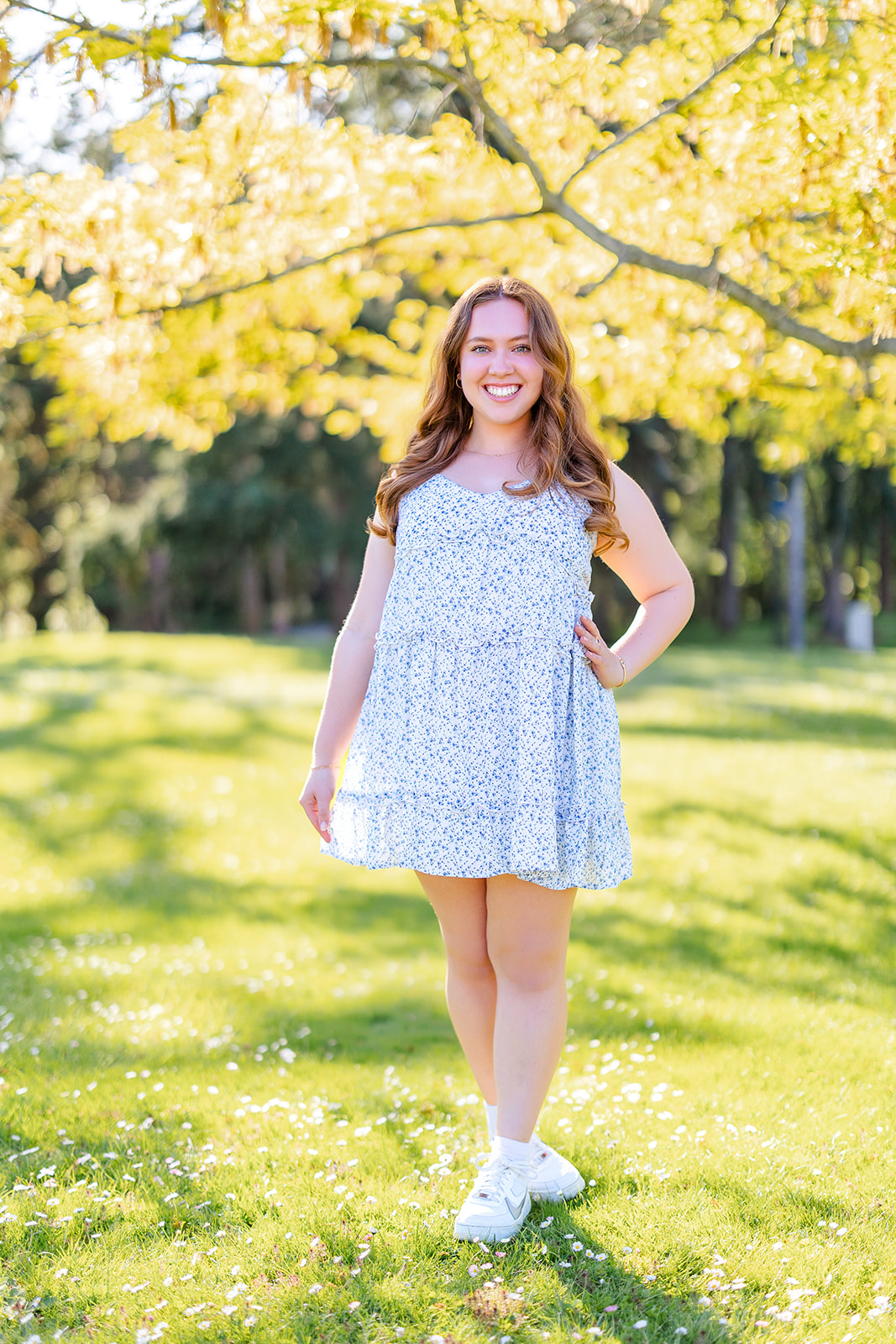 A high school senior in a blue dress smiles under a yellow tree after visiting college fairs in Seattle