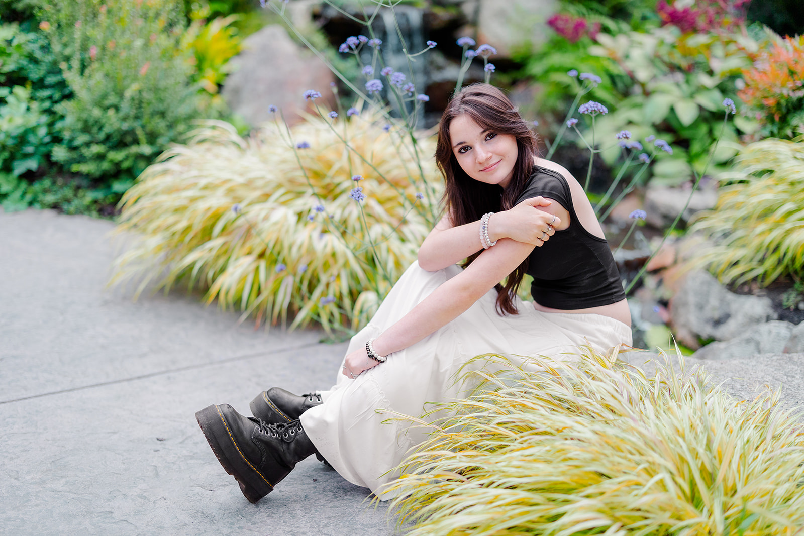 A high school senior sits in a flowering garden in a black top and white skirt after using CTE Dual Credit