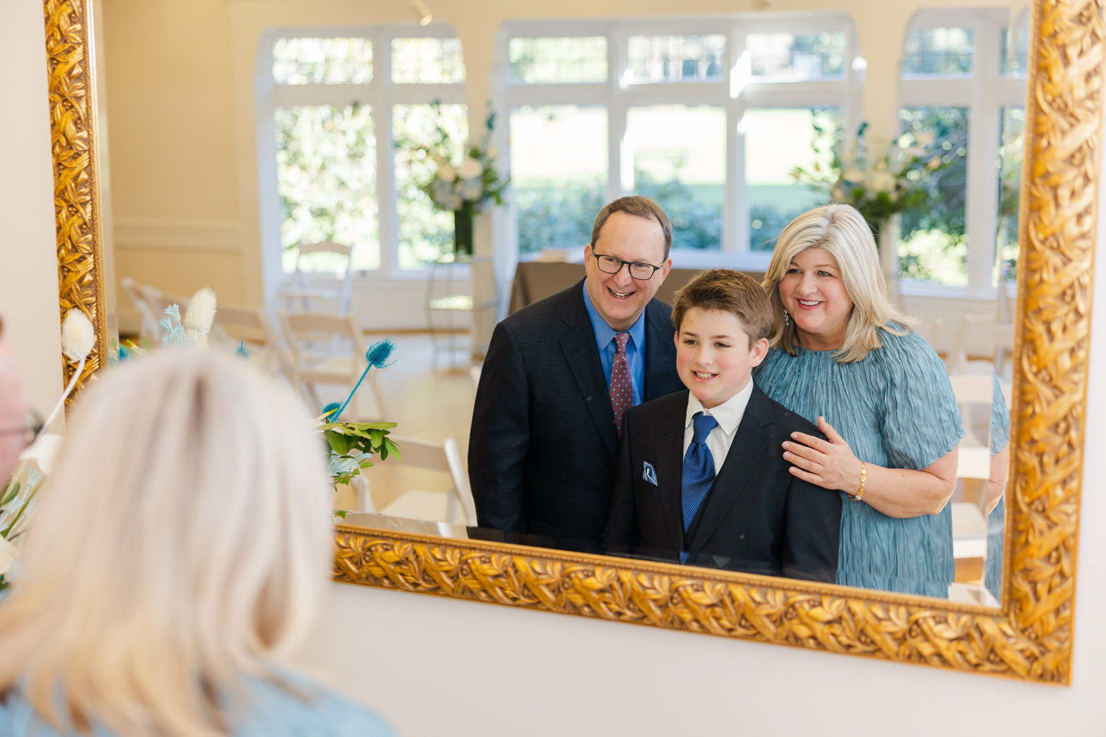 Happy mom and dad stand with their teen son in a mirror in suits and dress after using custom invitations in Seattle