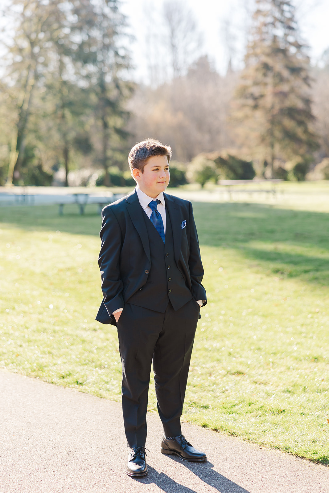 A teen boy stands in a sidewalk in a black suit with hands in pockets after using custom invitations in Seattle