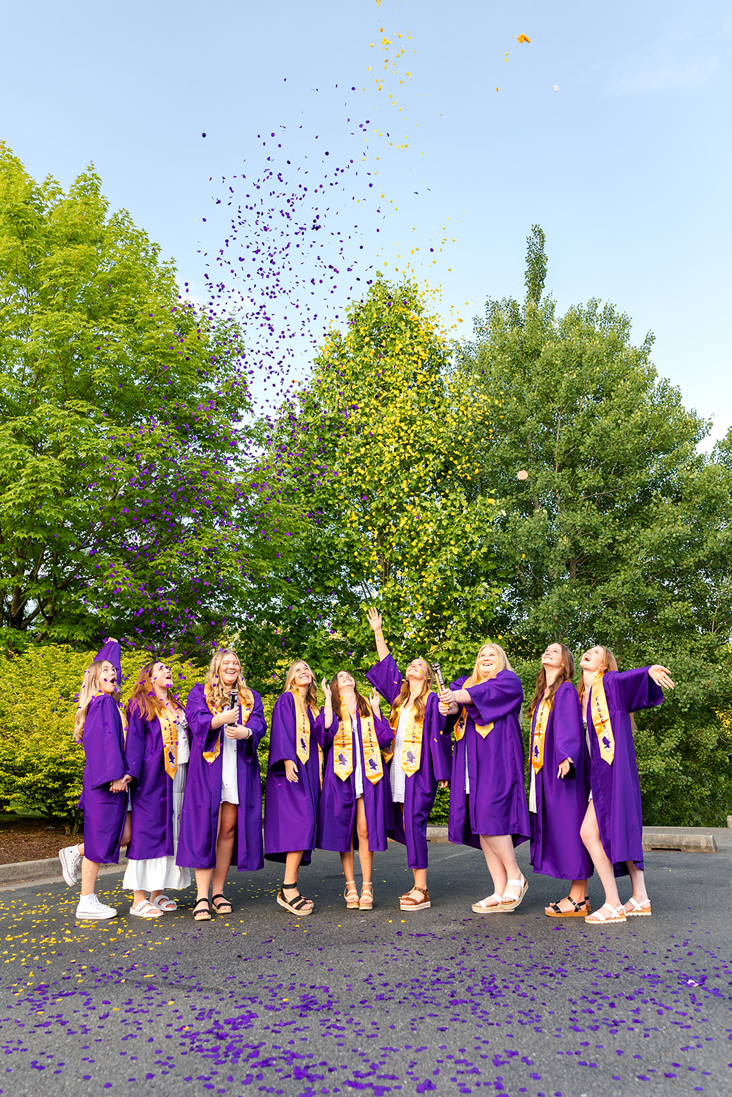 A group of graduates in purple robes pop confetti poppers in a parking lot before attending Grad Nights Seattle