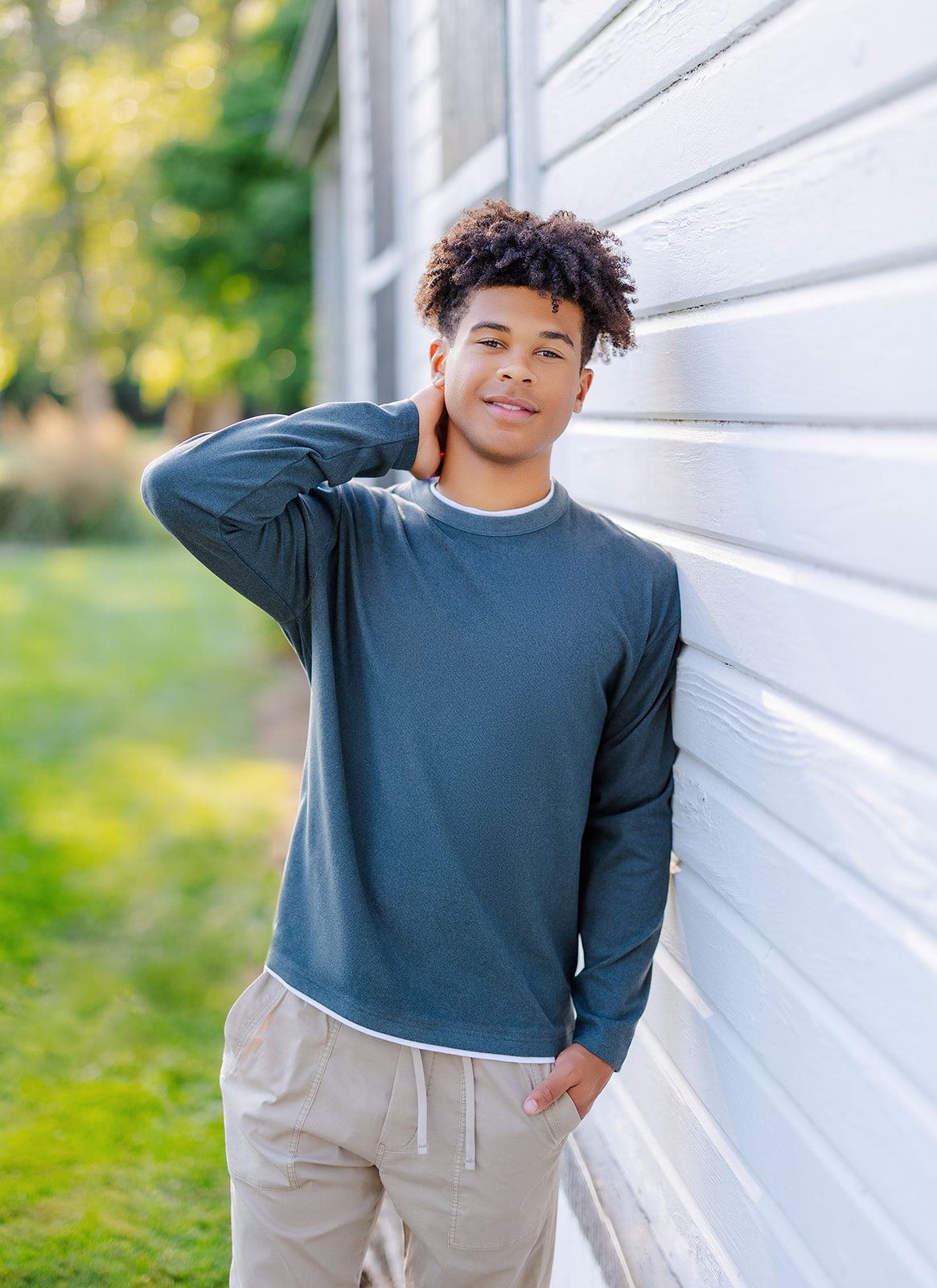 A teenager in a blue shirt leans on a house with a hand behind his neck after visiting graduation party venues in Seattle