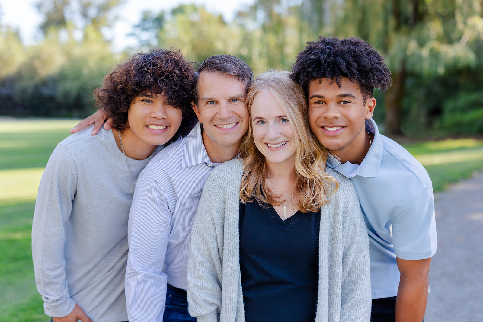 A happy family of four hugs and smiles in a park path after exploring graduation party venues in Seattle