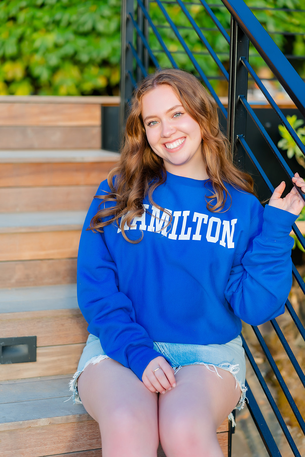 A happy teenager sits on stairs in a blue sweatshirt smiling