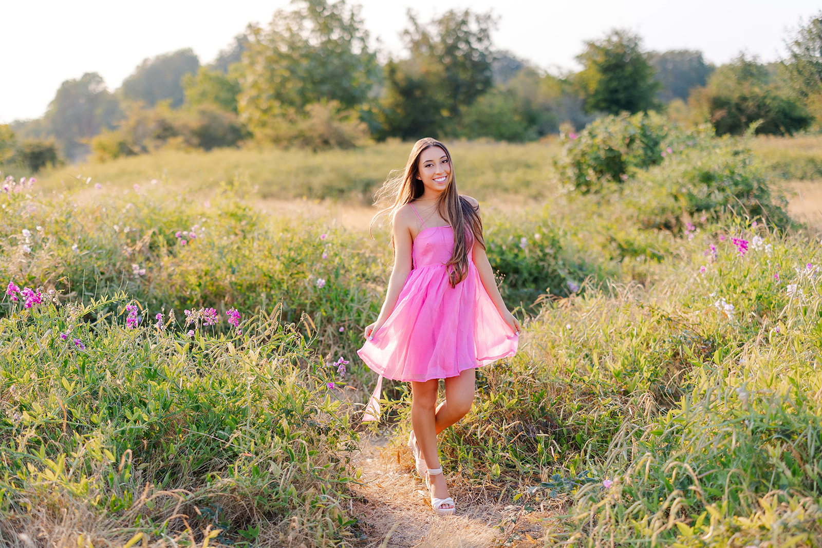 A teenage girl in a pink dress walks through a field of wildflowers at sunset after finding high school internships in Seattle