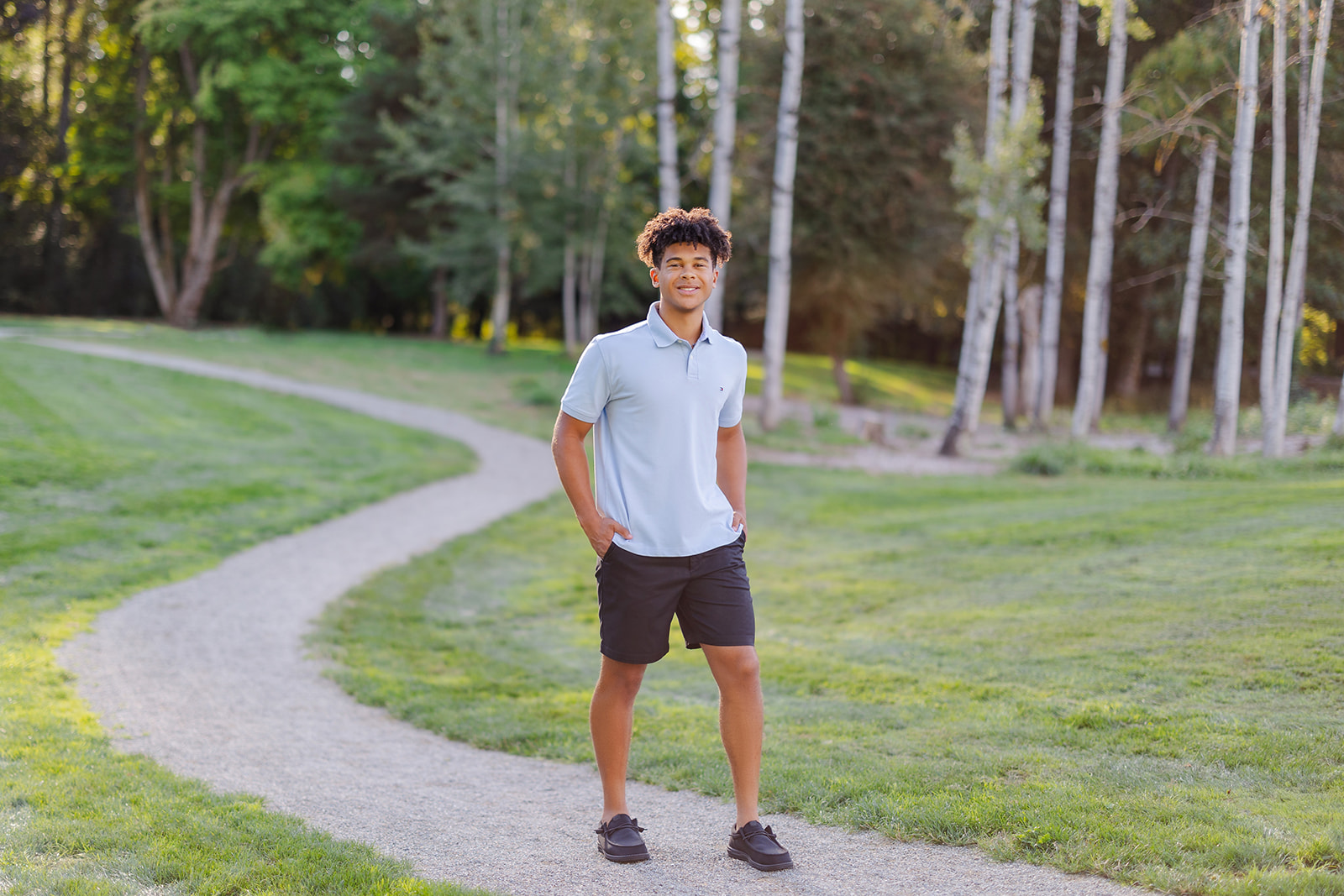 A high school senior in a blue shirt and loafers walk in a park trail with hands in pockets after finding scholarships in Seattle