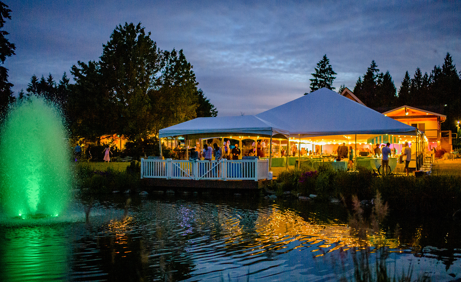 A look at an active reception party by a pond under a large tent