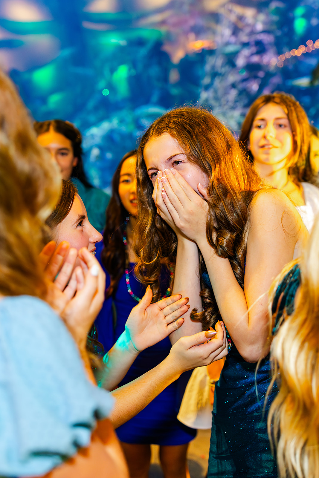 A happy teen girl covers her face while celebrating with friends at the aquarium
