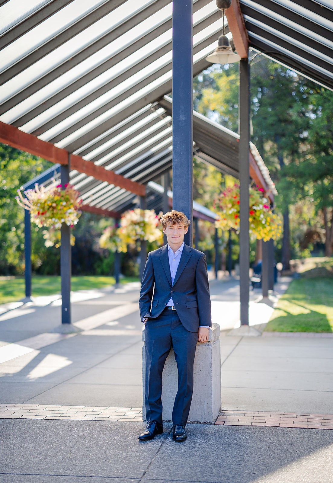 A high school senior in a blue suit leans on an overhang support beam after enjoying volunteer opportunities in Bellevue
