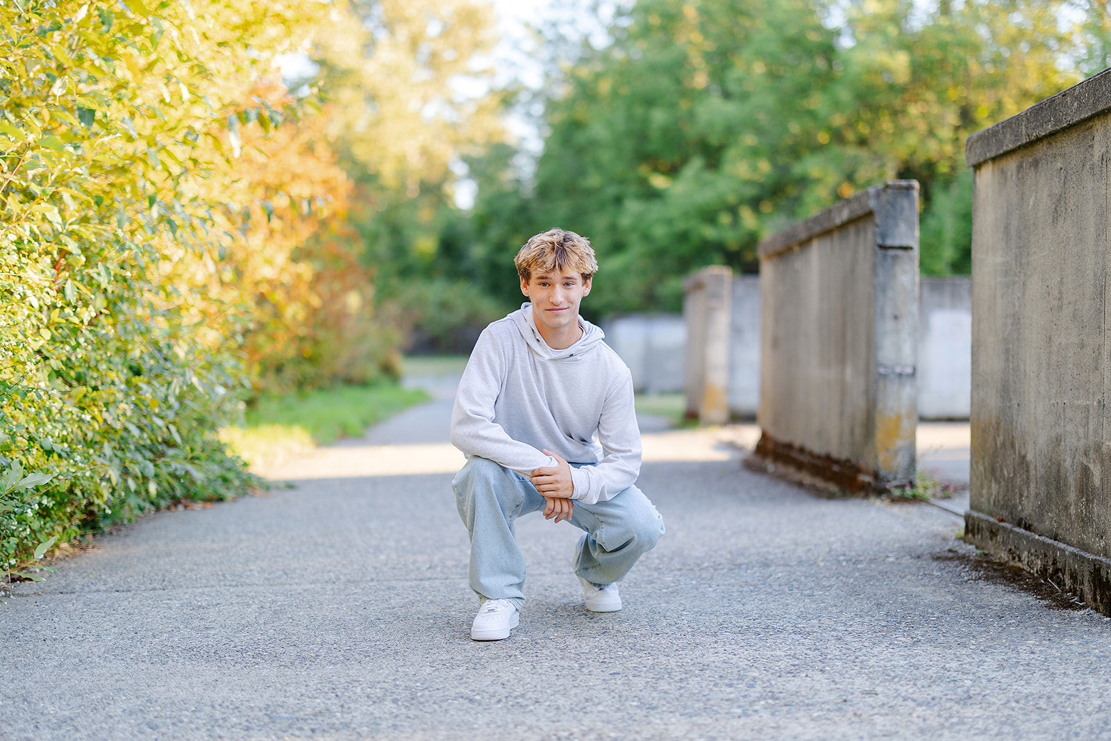 A high school senior squats in a park sidewalk in a grey hoodie and light jeans after finding volunteer opportunities in Bellevue