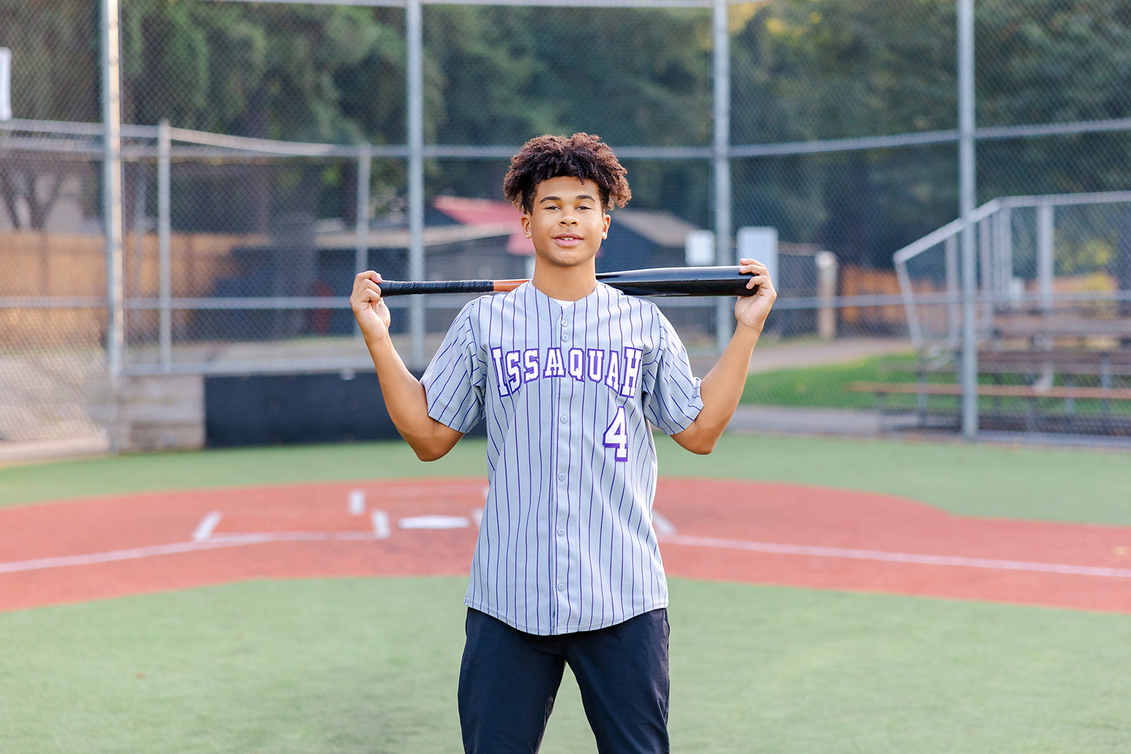 An Issaquah high school baseball player stands on the field holding his bat over his shoulders after enjoying volunteer opportunities in Issaquah