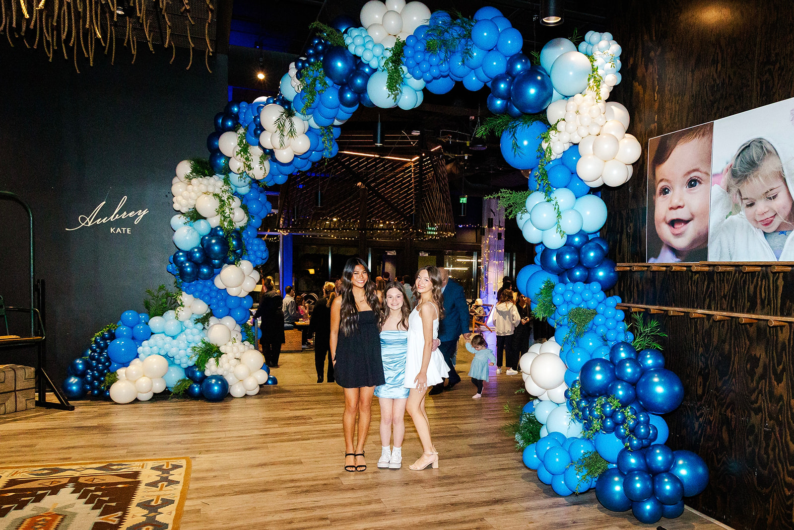 A young girl stands under a massive balloon arch with two friends at her bat mitzvah